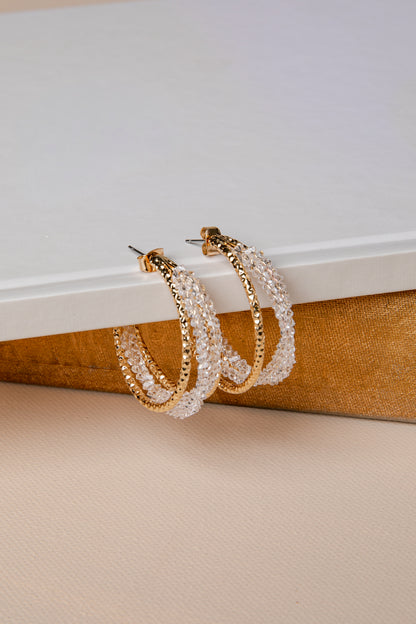Pair of gold and pearl hoop earrings on a textured surface with a neutral background