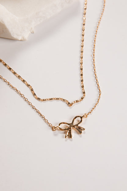 Gold necklace with a bow pendant on a light background