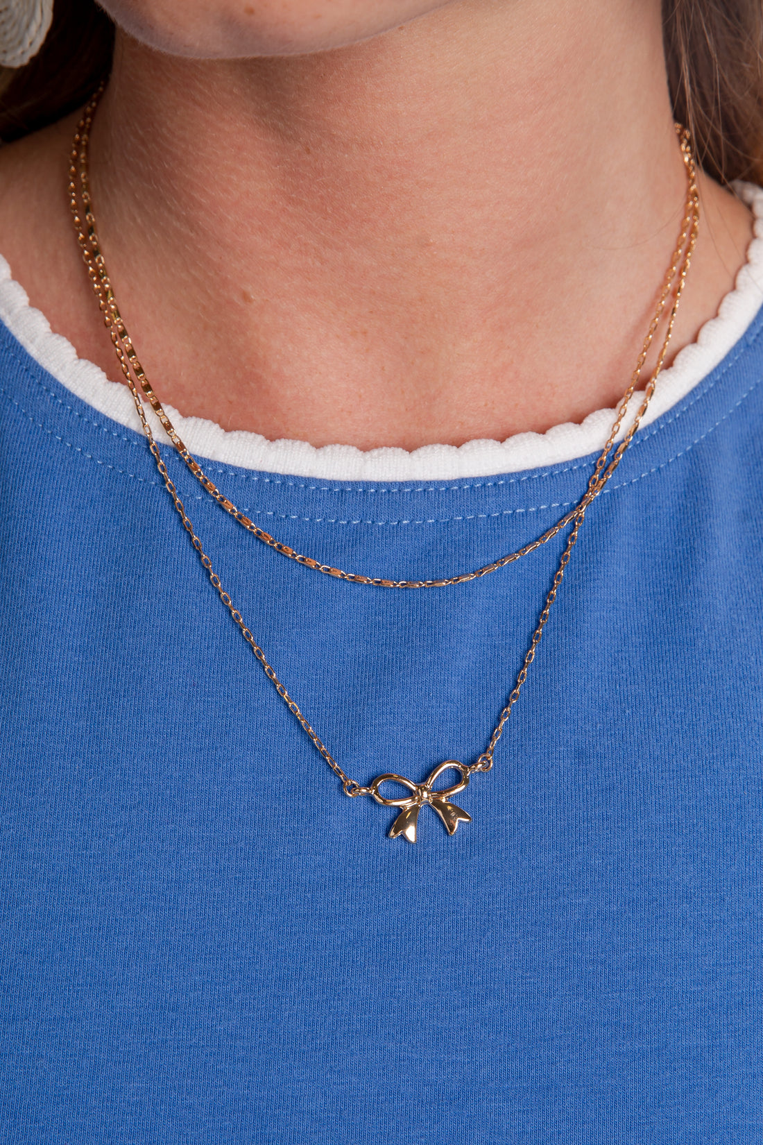 Gold necklace with a bow pendant worn by a person on a blue shirt.