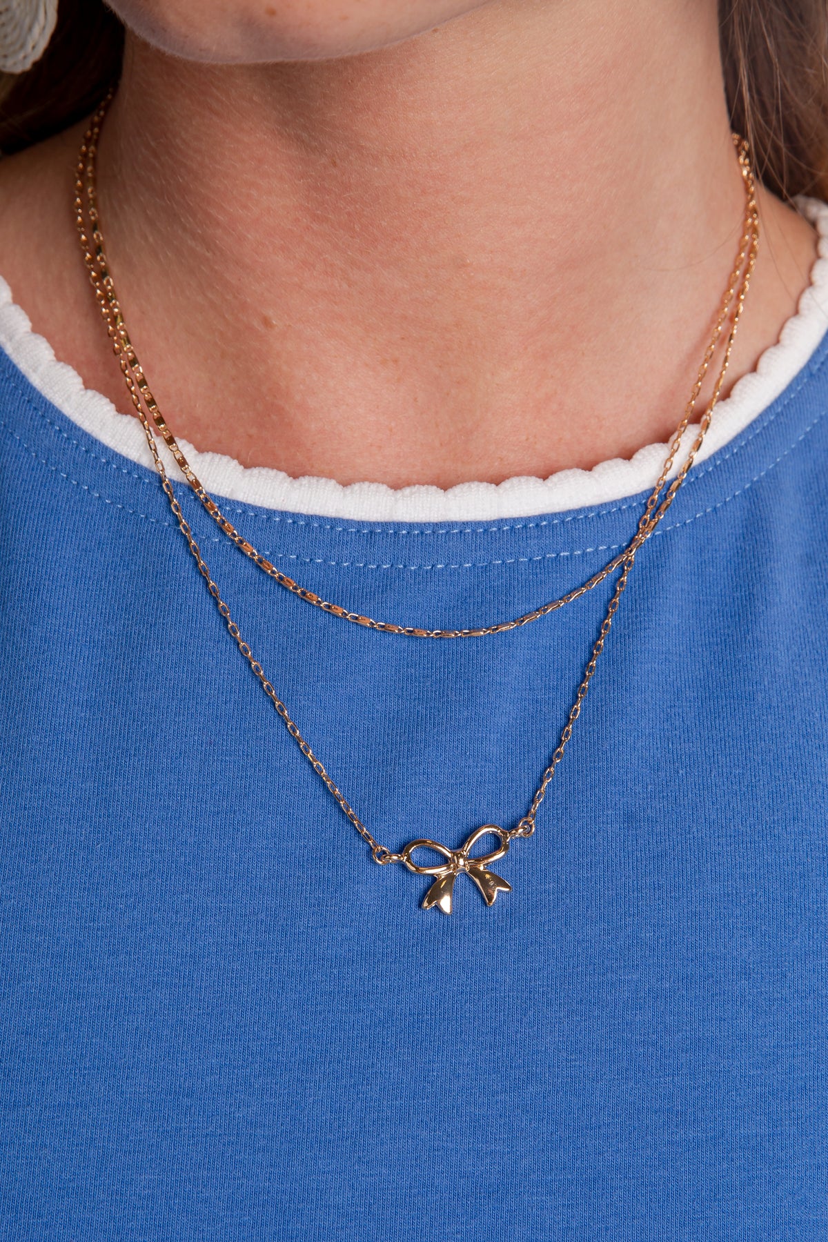 Gold necklace with a bow pendant worn by a person on a blue shirt.