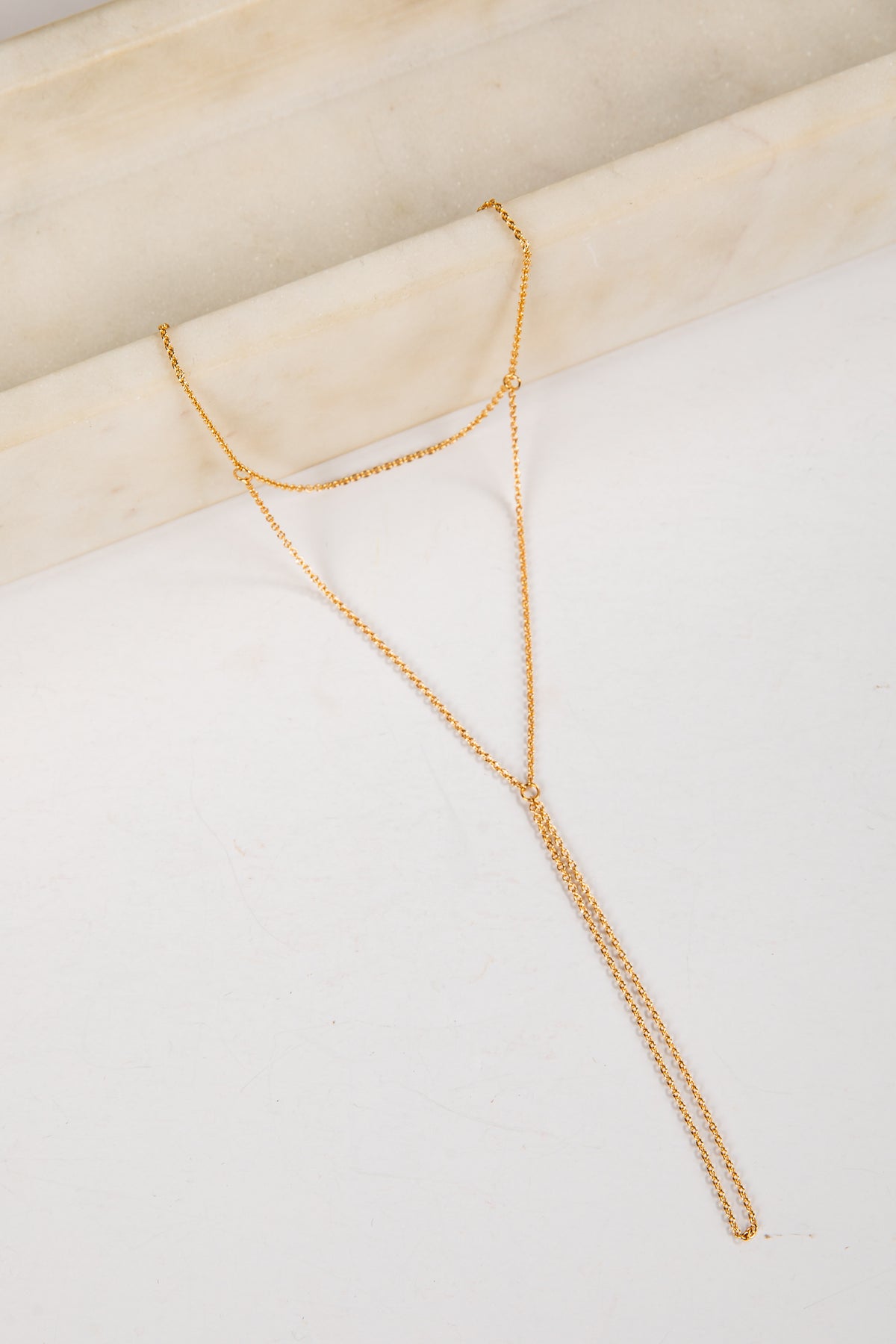 Gold necklace on a white surface with a beige background