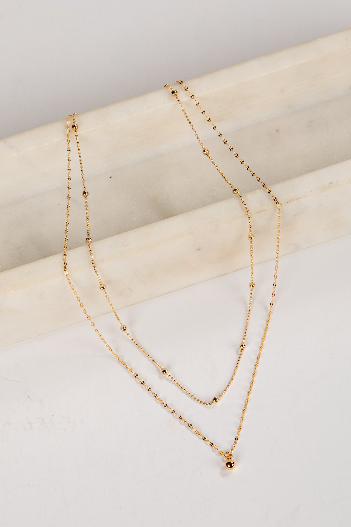 Two gold necklaces on a light wooden surface