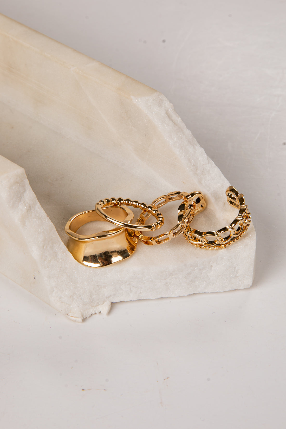 four gold rings on a white stone surface