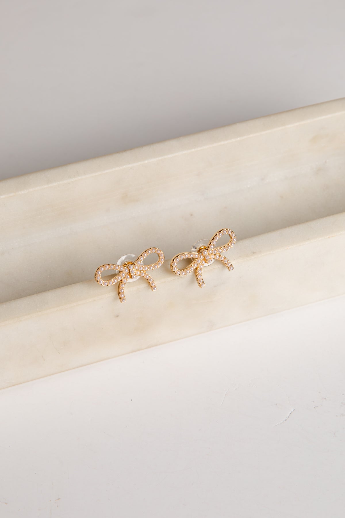 Gold bow-shaped earrings on a marble surface