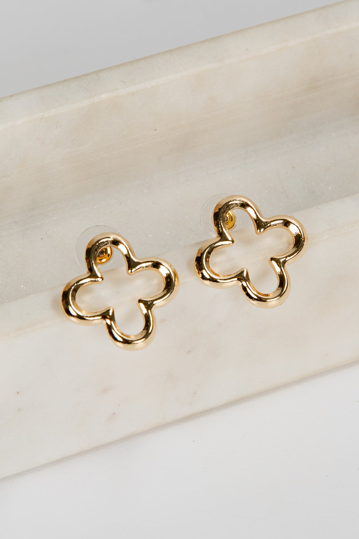 Gold four-leaf clover earrings on a white marble surface