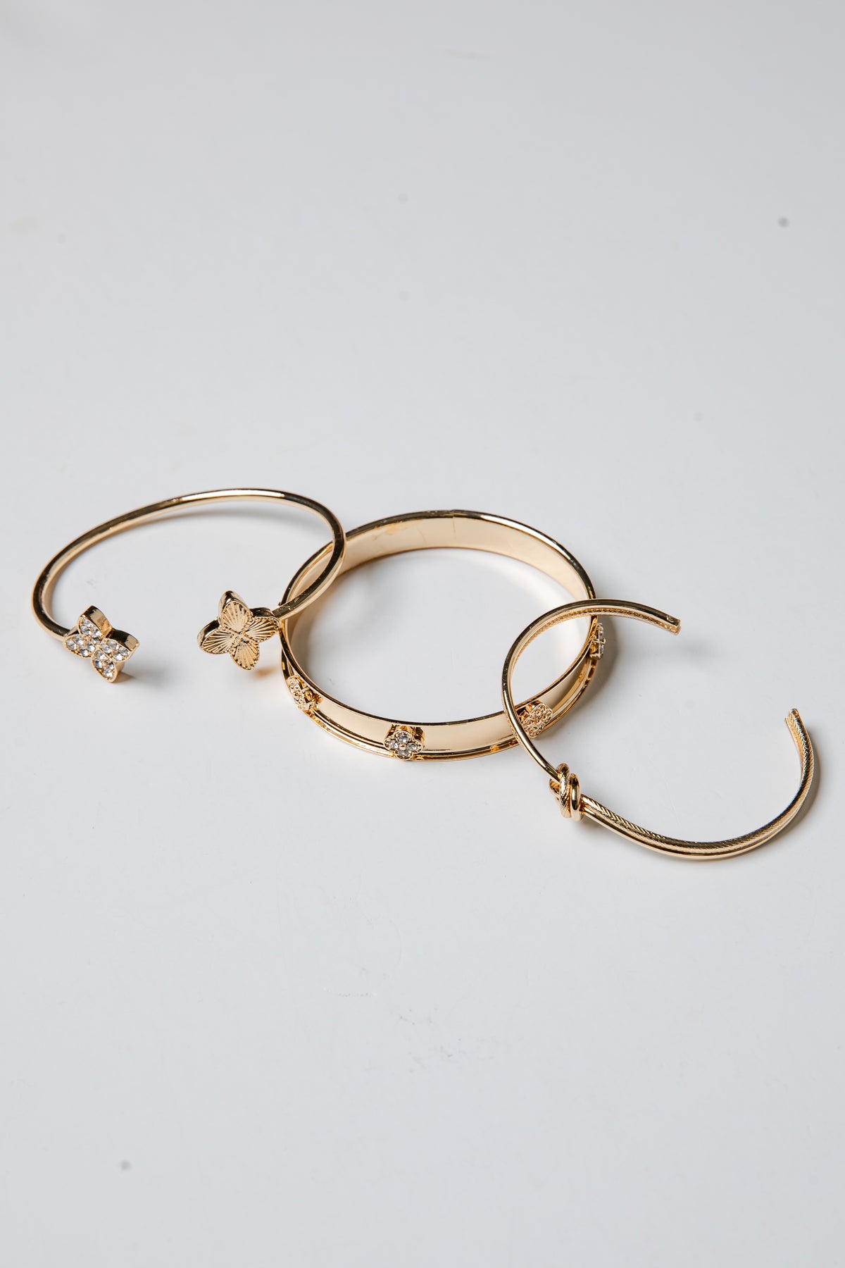 Three gold bracelets with decorative elements on a light gray background