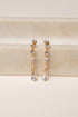 Gold and silver drop earrings on a beige surface