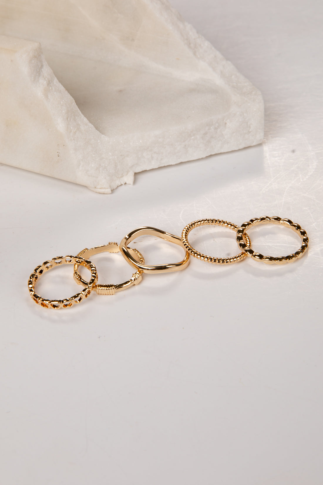 Set of gold rings on a white surface with a beige stone block in the background