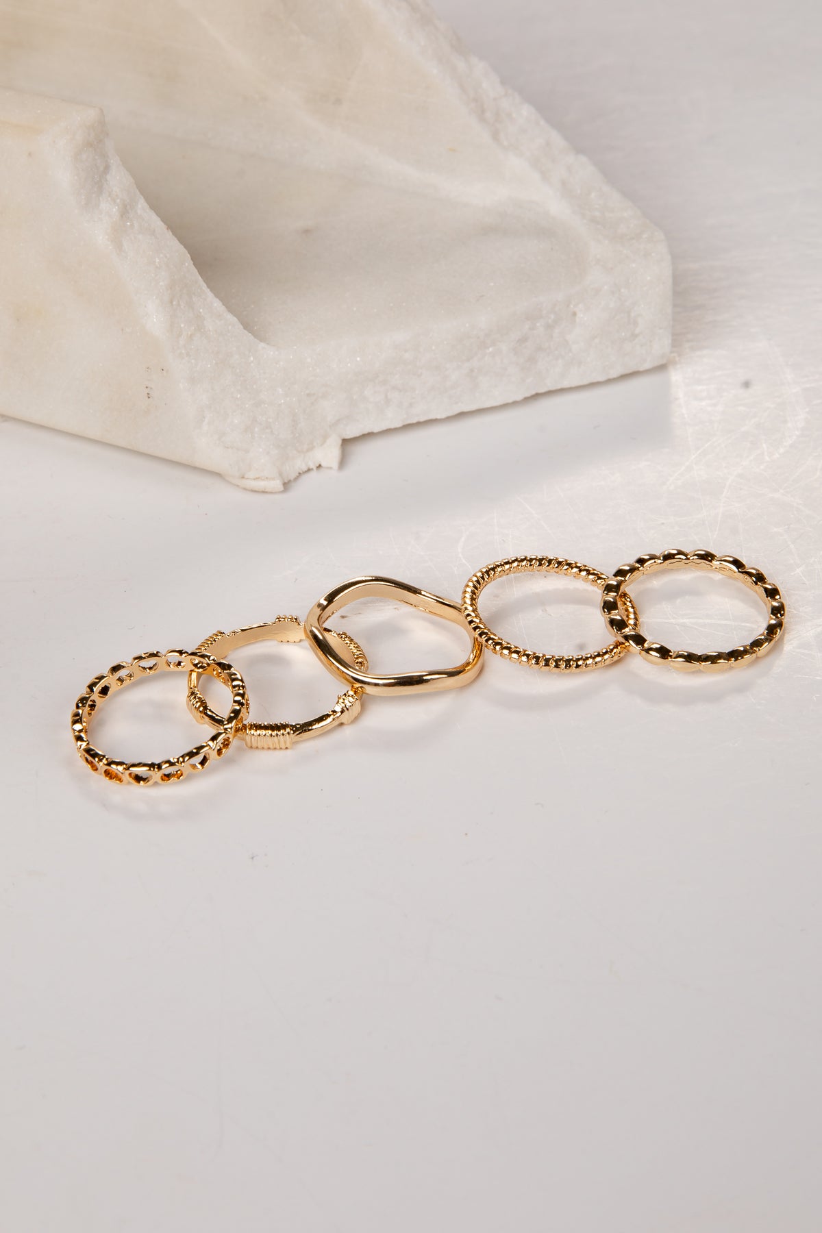 Set of gold rings on a white surface with a beige stone block in the background