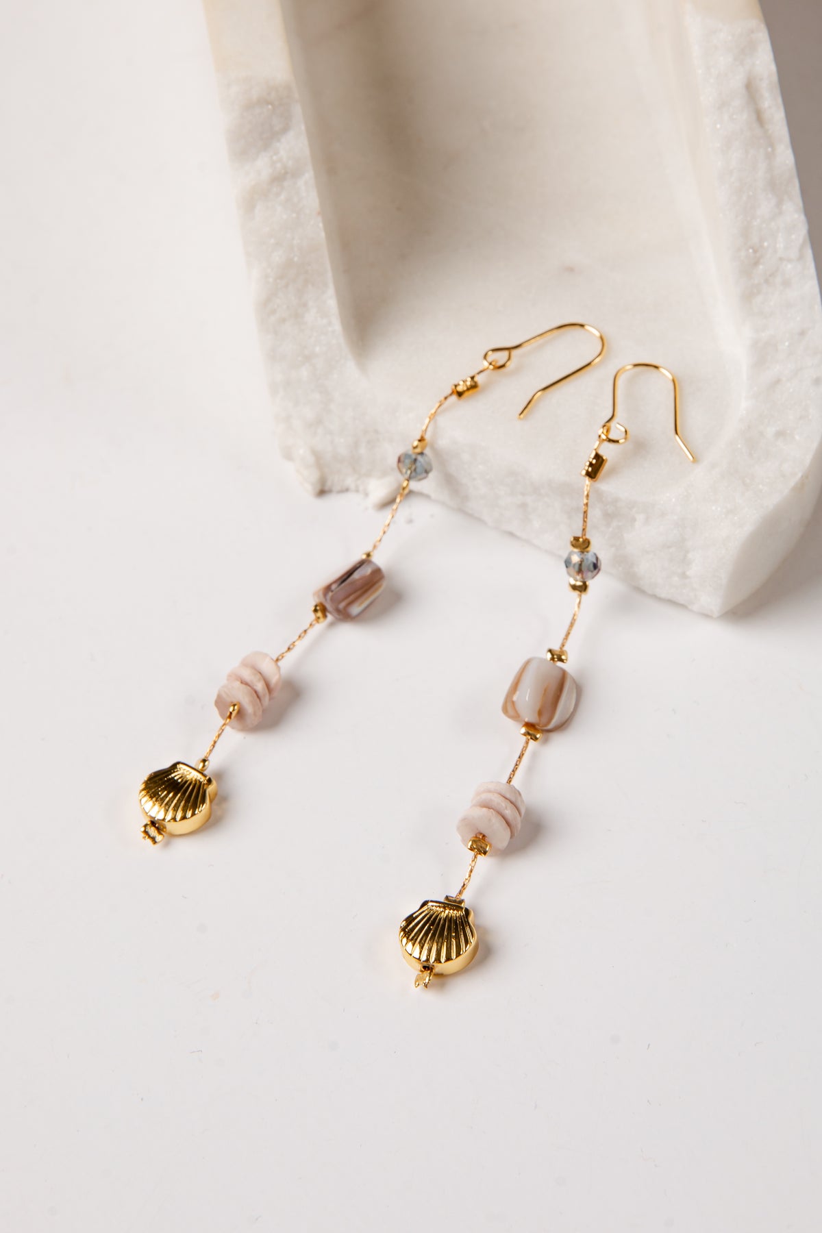 Gold earrings with shell and bead details on a white surface