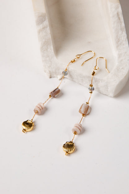 Gold earrings with shell and bead details on a white surface