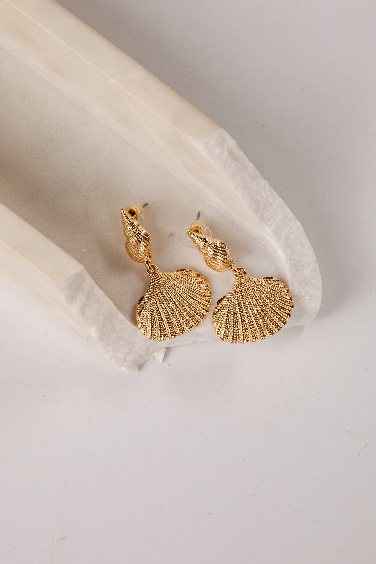 Gold shell-shaped earrings on a light stone surface