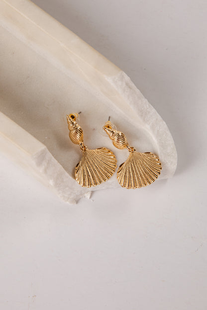 Gold shell-shaped earrings on a light stone surface