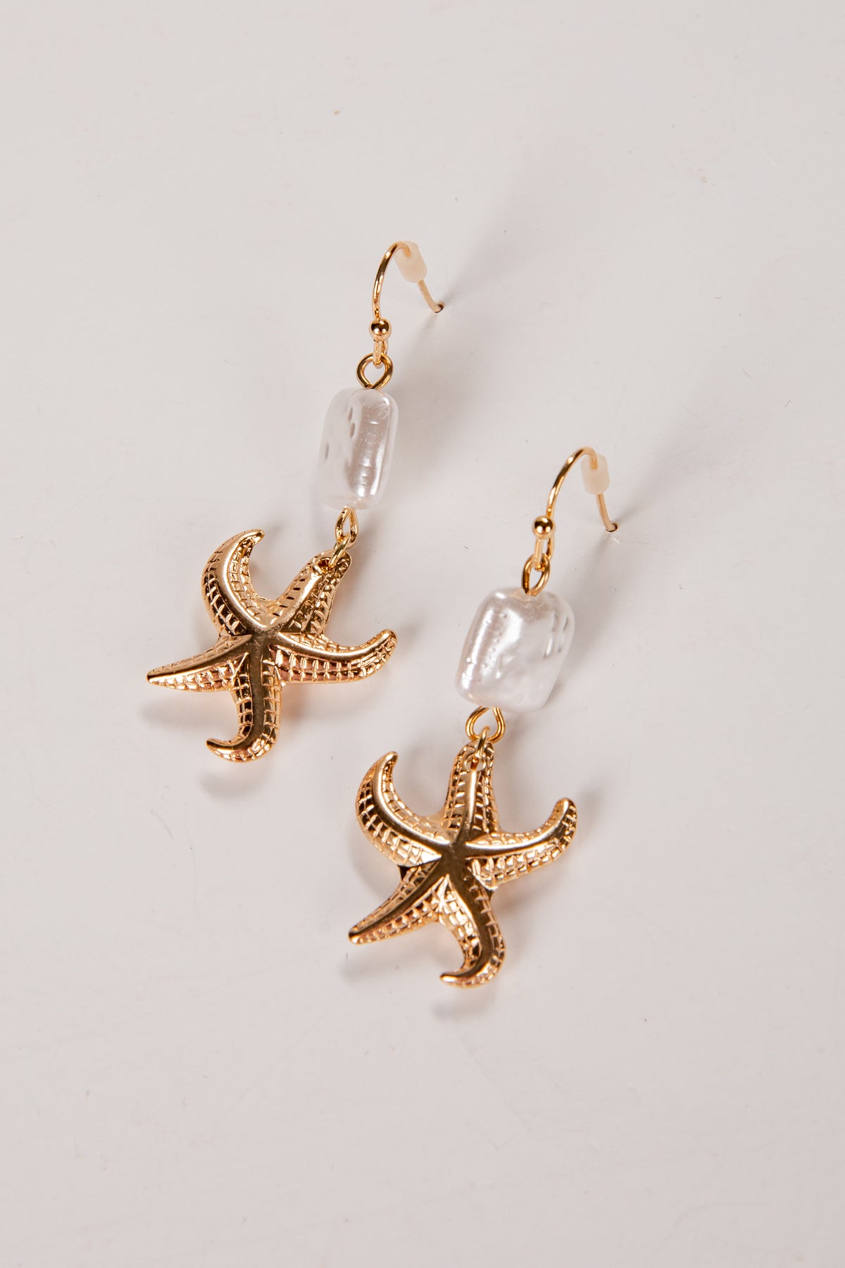 Gold starfish earrings on a light gray background