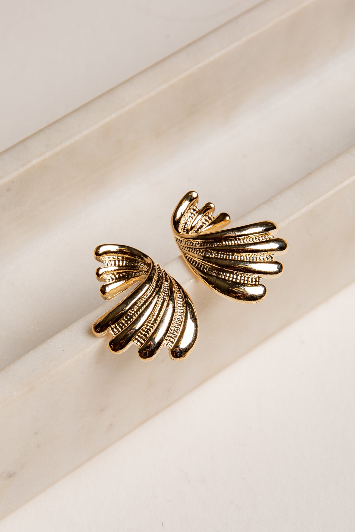 Gold leaf-shaped earrings on a light beige background