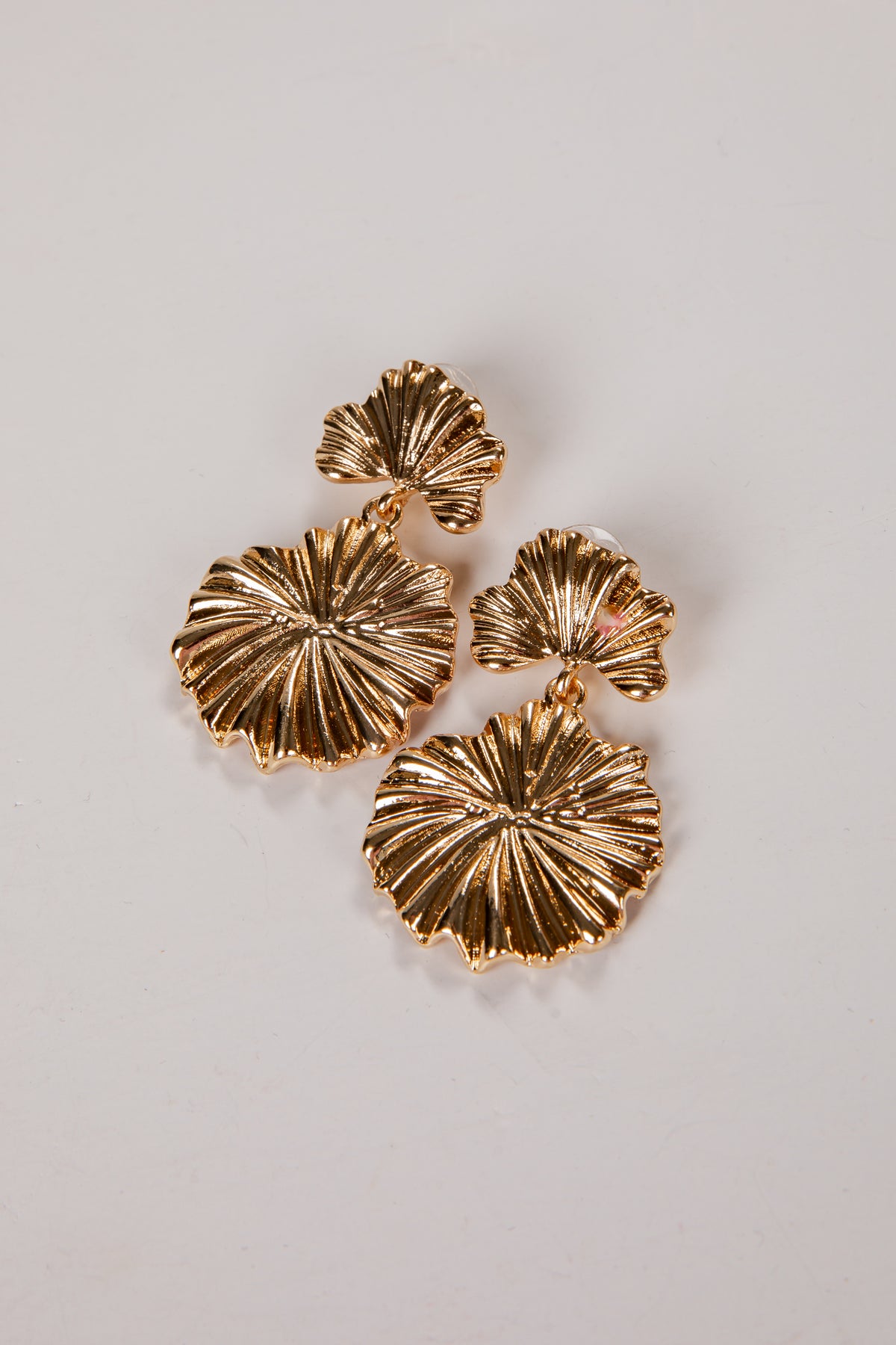 Gold leaf-shaped earrings on a light gray background