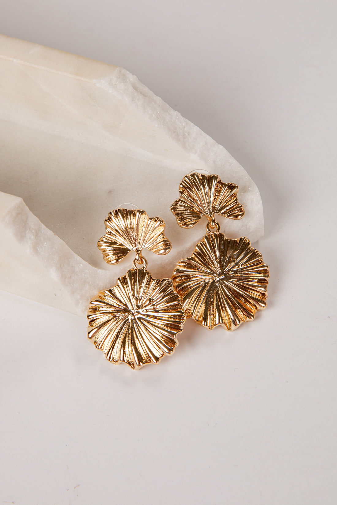 Gold leaf-shaped earrings on a white stone surface