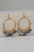 Gold hoop earrings with blue and green gemstone drops on a light background