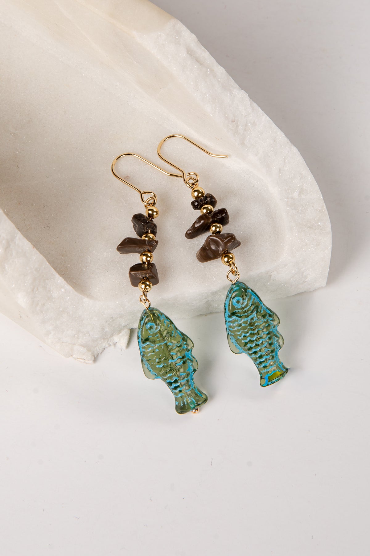 Pair of earrings with turquoise fish-shaped drops and brown beads on a white stone background