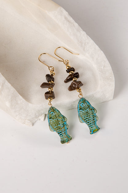 Pair of earrings with turquoise fish-shaped drops and brown beads on a white stone background