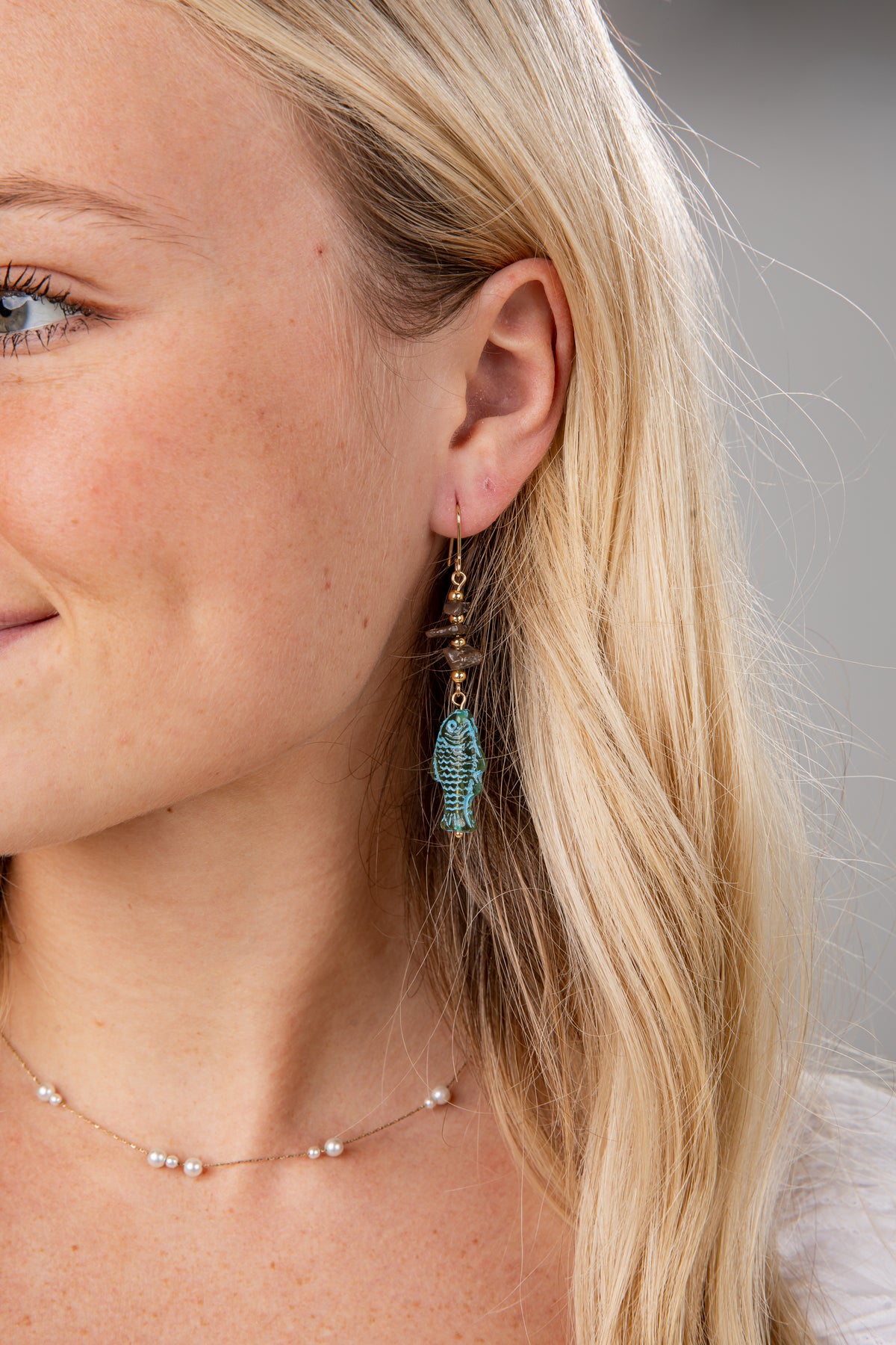 Close-up of a woman wearing turquoise earrings with a neutral background