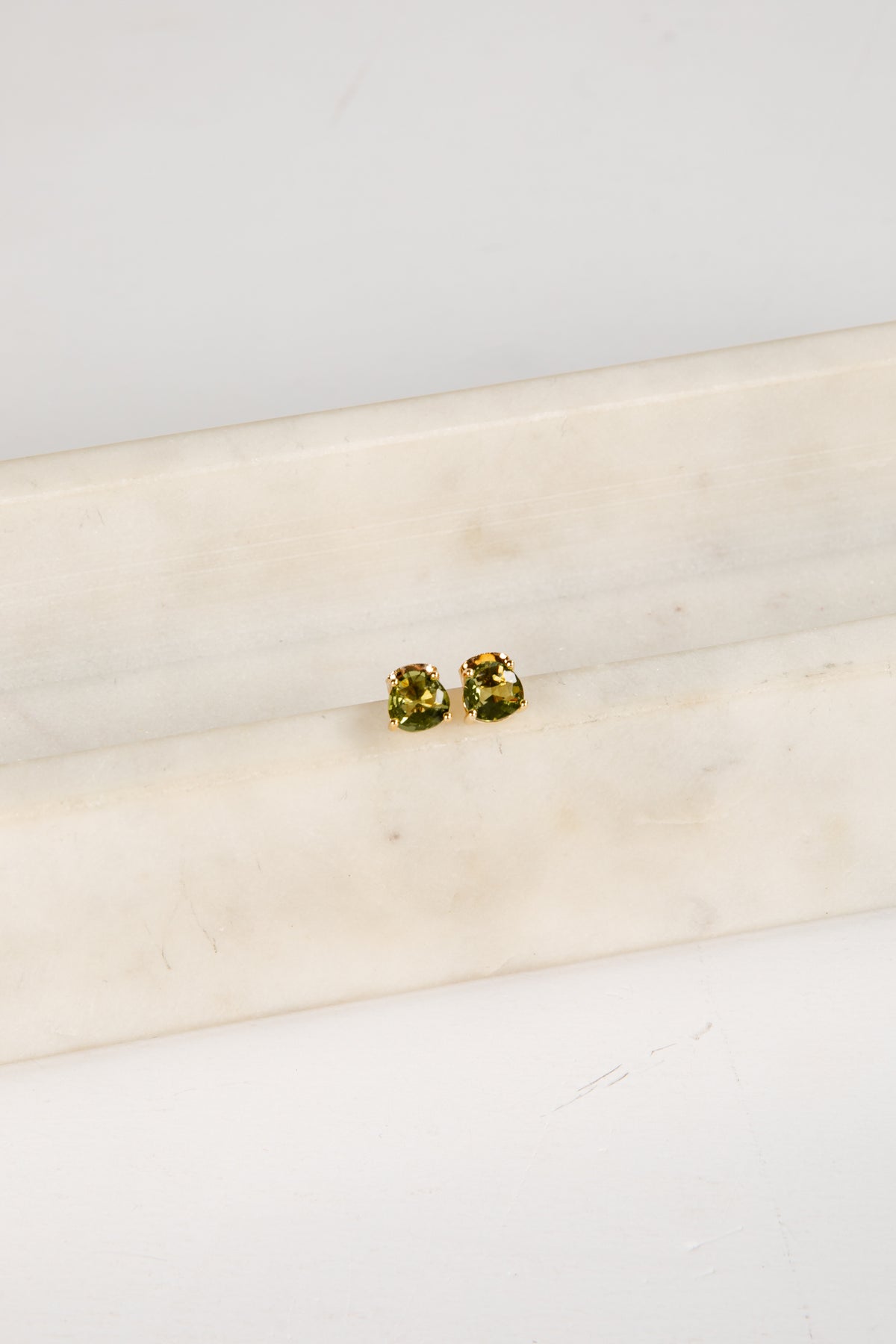 Pair of green gemstone stud earrings on a white marble surface