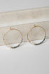 Gold hoop earrings with gray beads on a marble surface