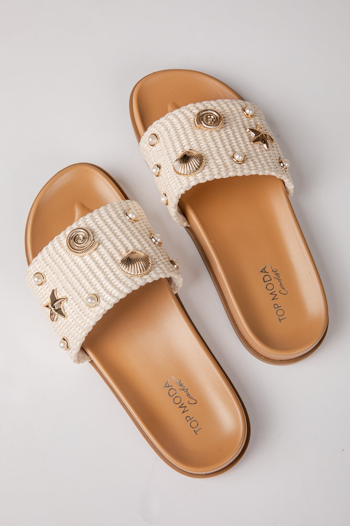Pair of beige sandals with decorative straps on a light gray background
