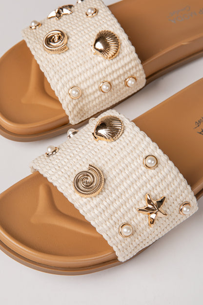 White sandals with gold embellishments on a white background