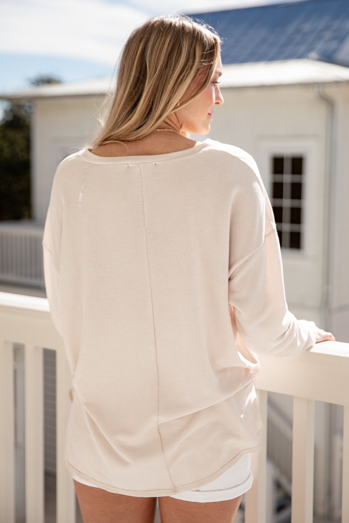 Woman wearing a beige long-sleeve top and white shorts on a balcony.