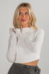 Woman wearing a white long-sleeve top against a plain background