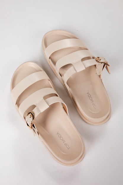 Pair of beige sandals with gold buckles on a light gray background