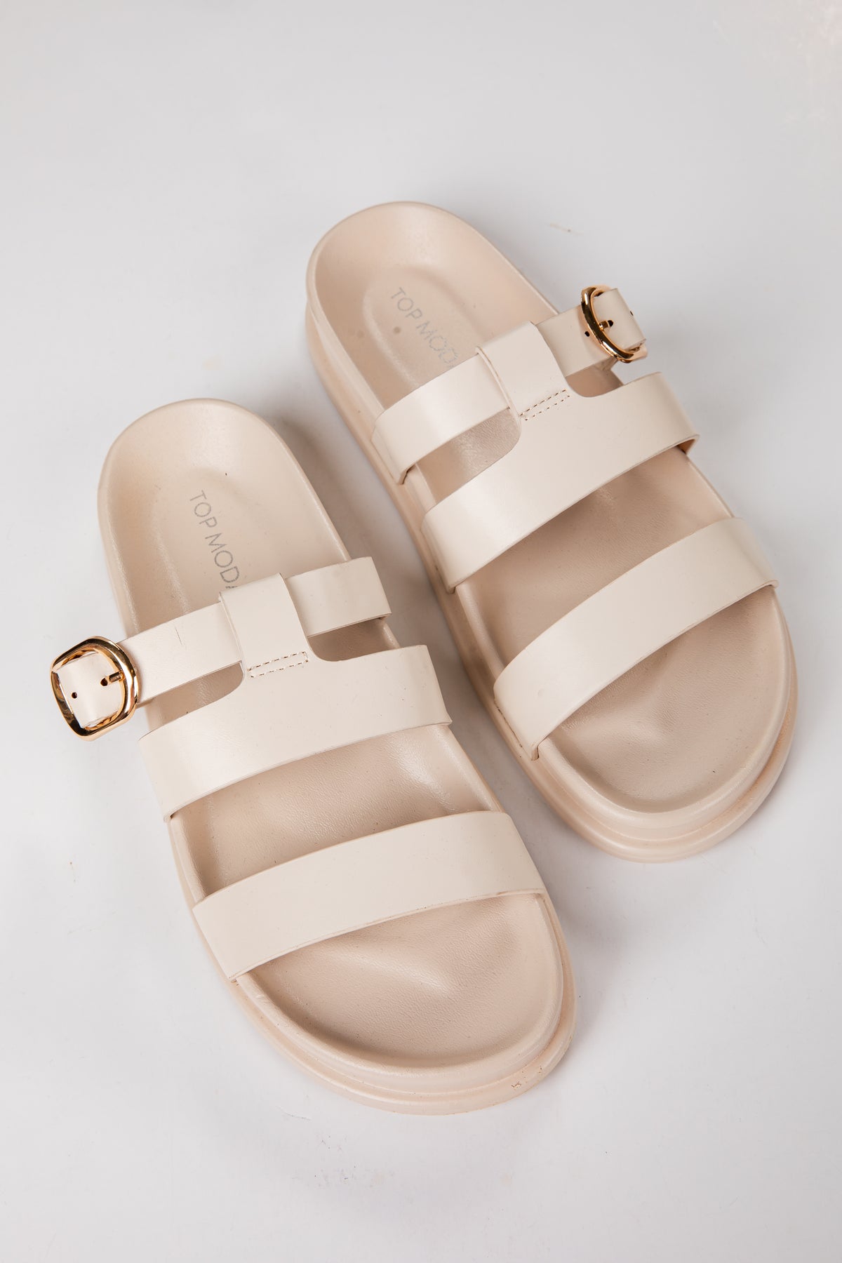 Beige sandals with gold buckles on a light gray background