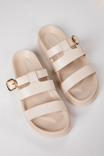Beige sandals with gold buckles on a light gray background