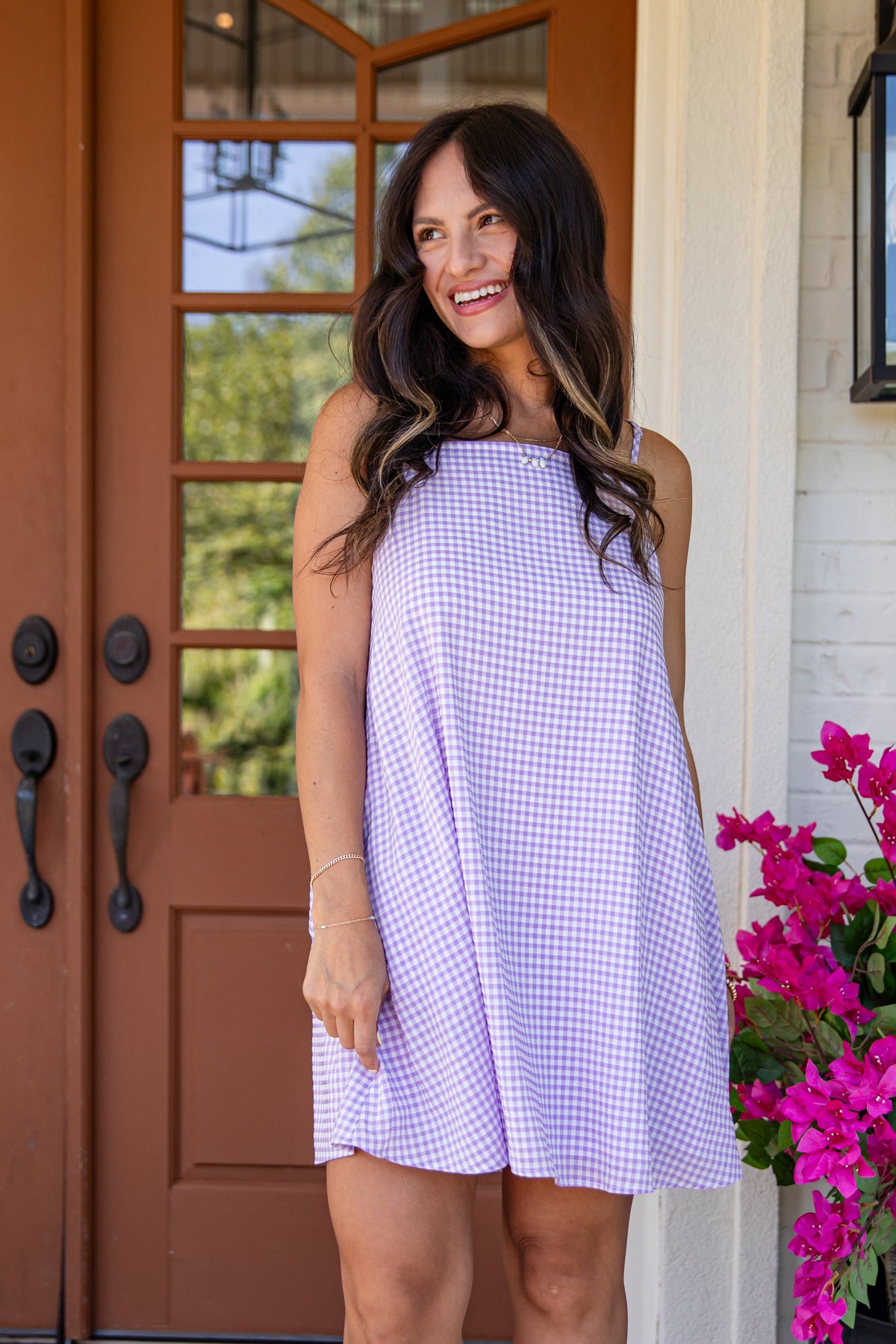 Woman in a purple checkered dress standing in front of a brown door with glass panels.