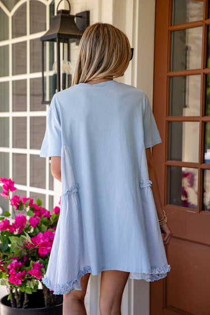 Woman wearing a light blue dress standing in front of a door with flowers and a lantern.