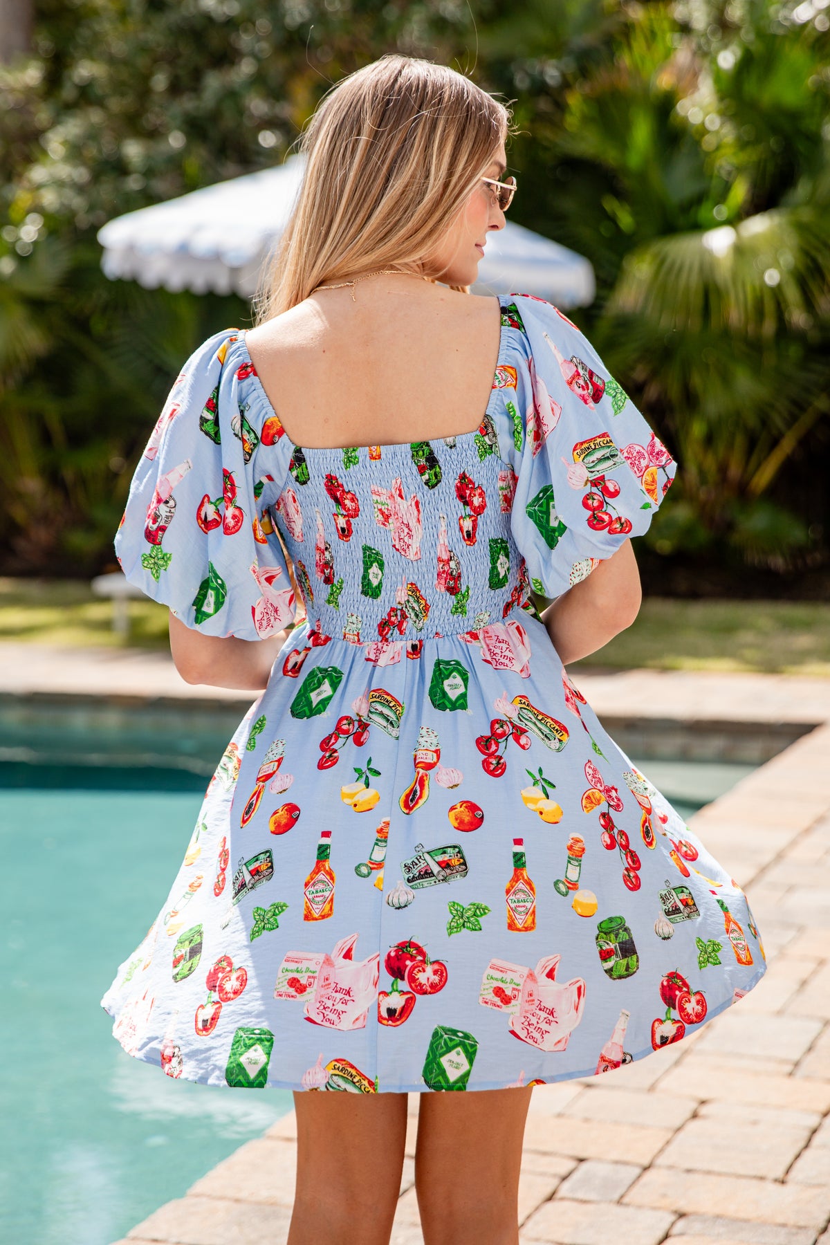 Woman wearing a colorful dress with a pattern of food items by a poolside.
