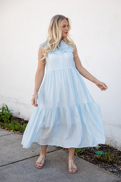Woman wearing a light blue dress standing against a white wall.