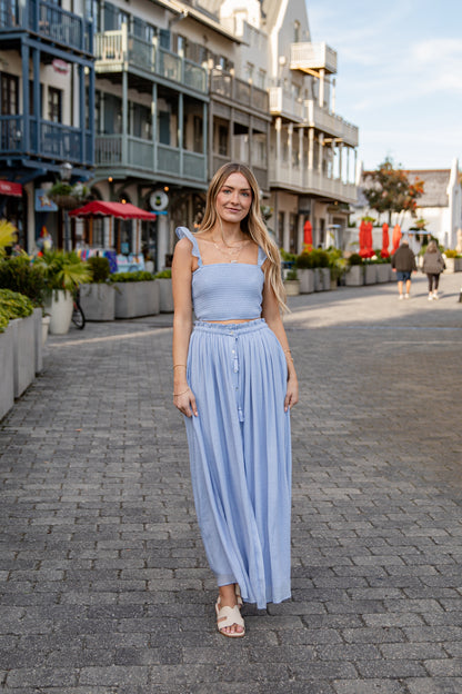 Woman in a light blue outfit standing on a street with buildings and people in the background