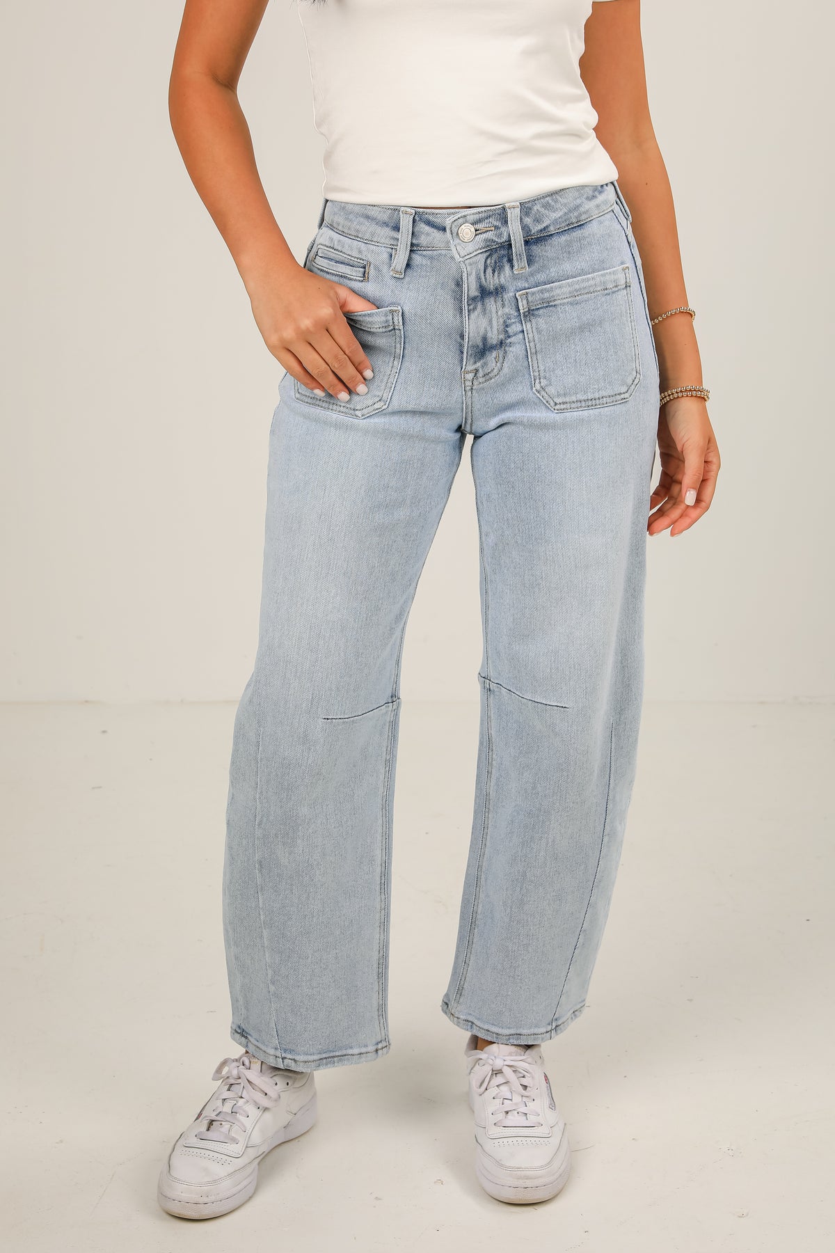 Person wearing light blue jeans and white sneakers on a plain background
