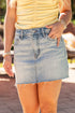 Person wearing a yellow top and denim skirt with bracelets on a blurred outdoor background