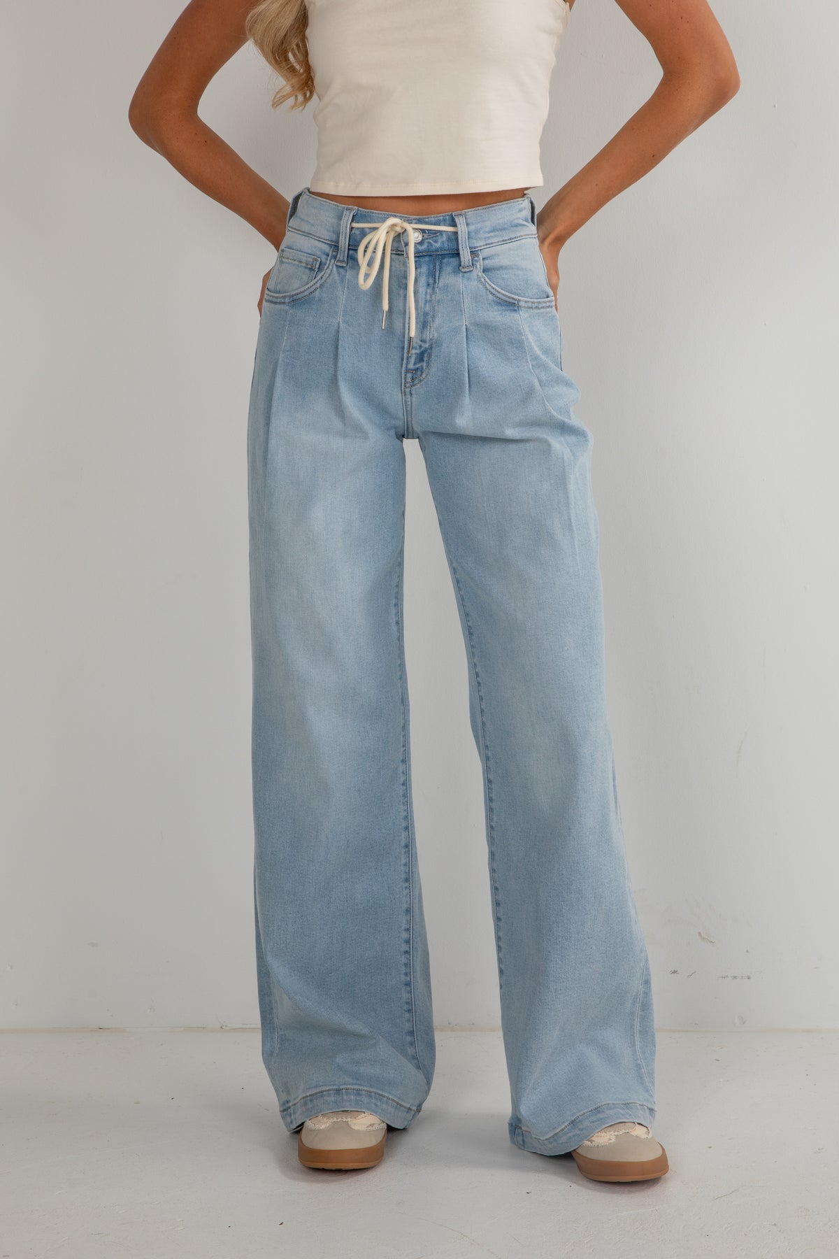 Person wearing light blue jeans and a white top on a plain background