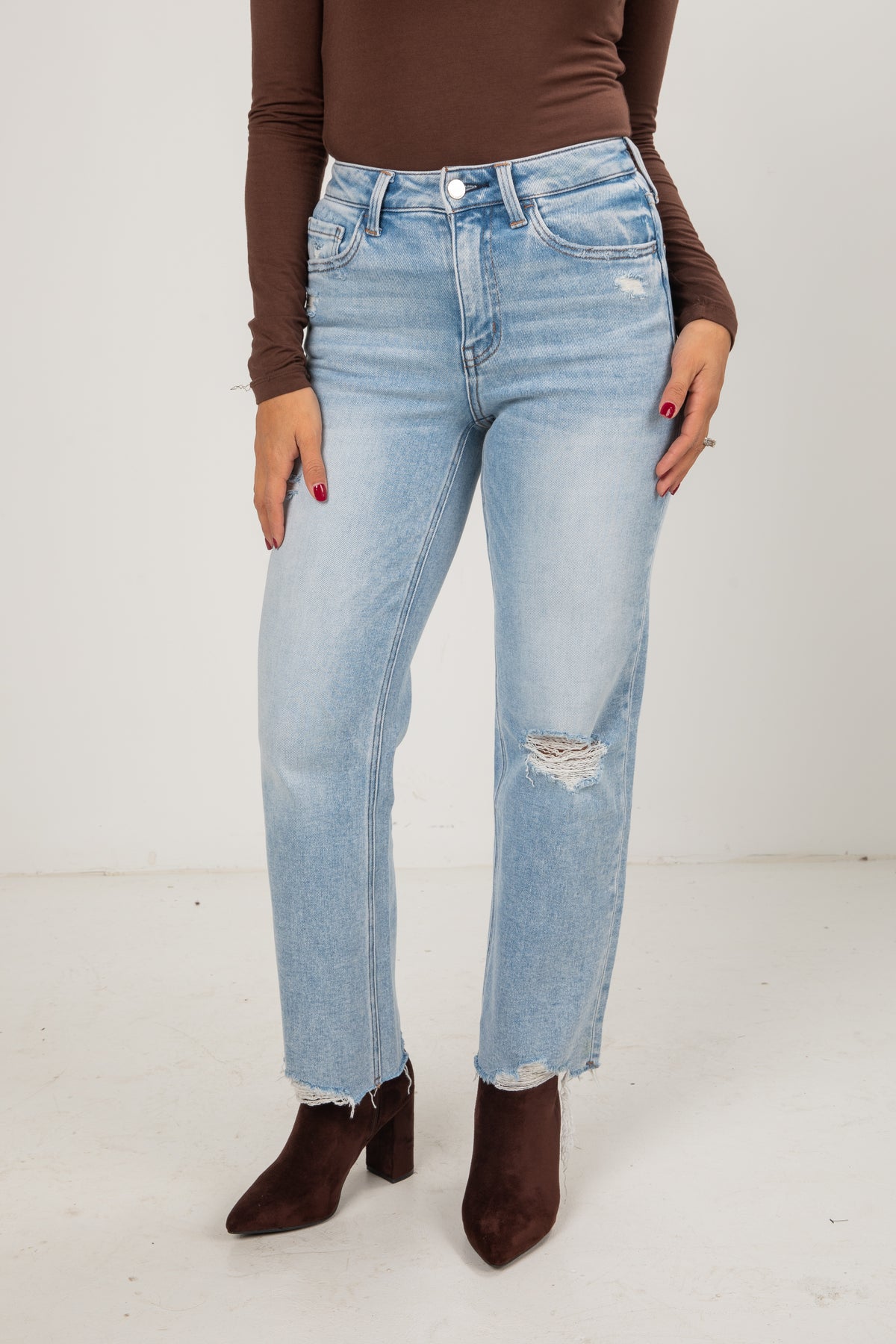 Person wearing light blue jeans and brown shoes on a white background
