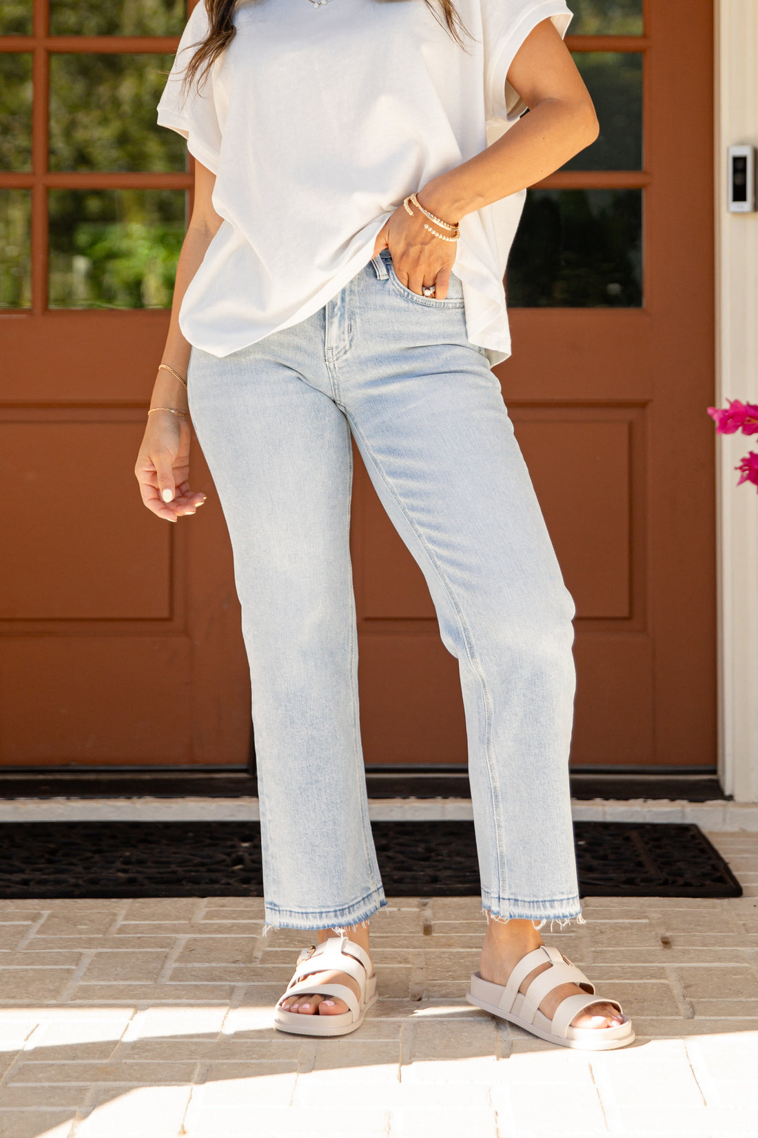 Person wearing light blue jeans and a white shirt standing on a porch.