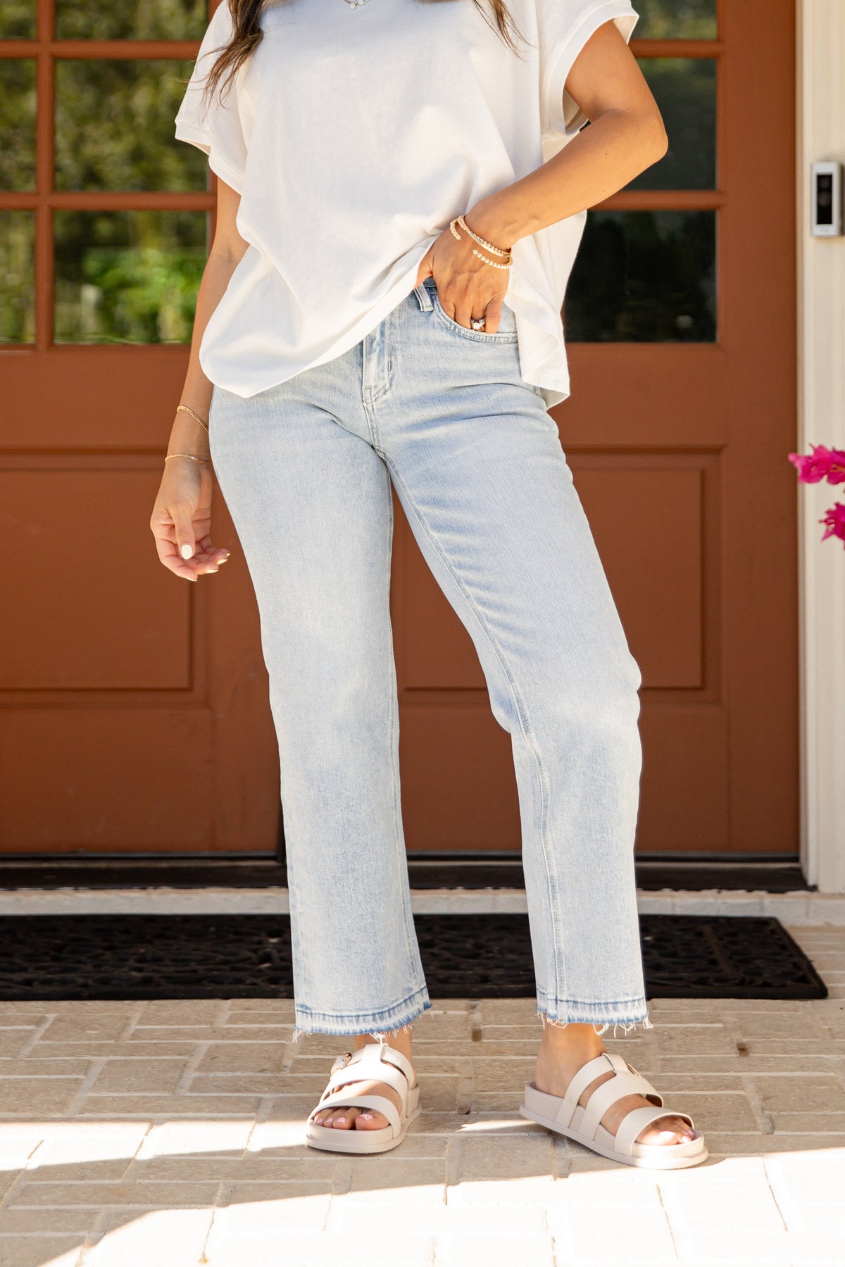 Person wearing light blue jeans and a white shirt standing on a porch.