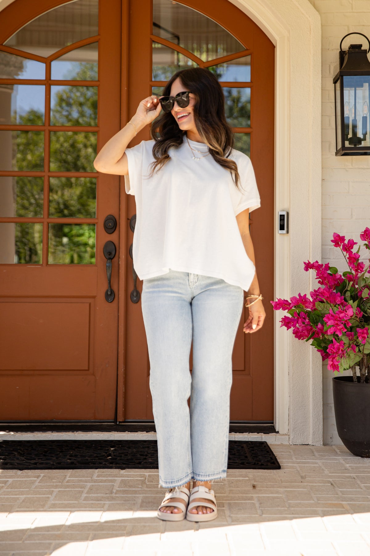 Woman standing in front of a brown door with pink flowers to her right