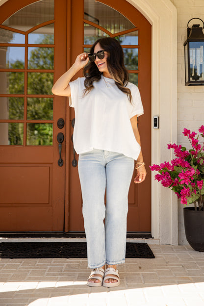 Woman standing in front of a brown door with pink flowers to her right