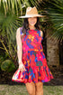 Woman wearing a colorful dress and straw hat standing in front of palm leaves.