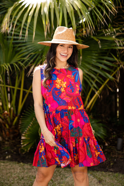 Woman wearing a colorful dress and straw hat standing in front of palm trees.