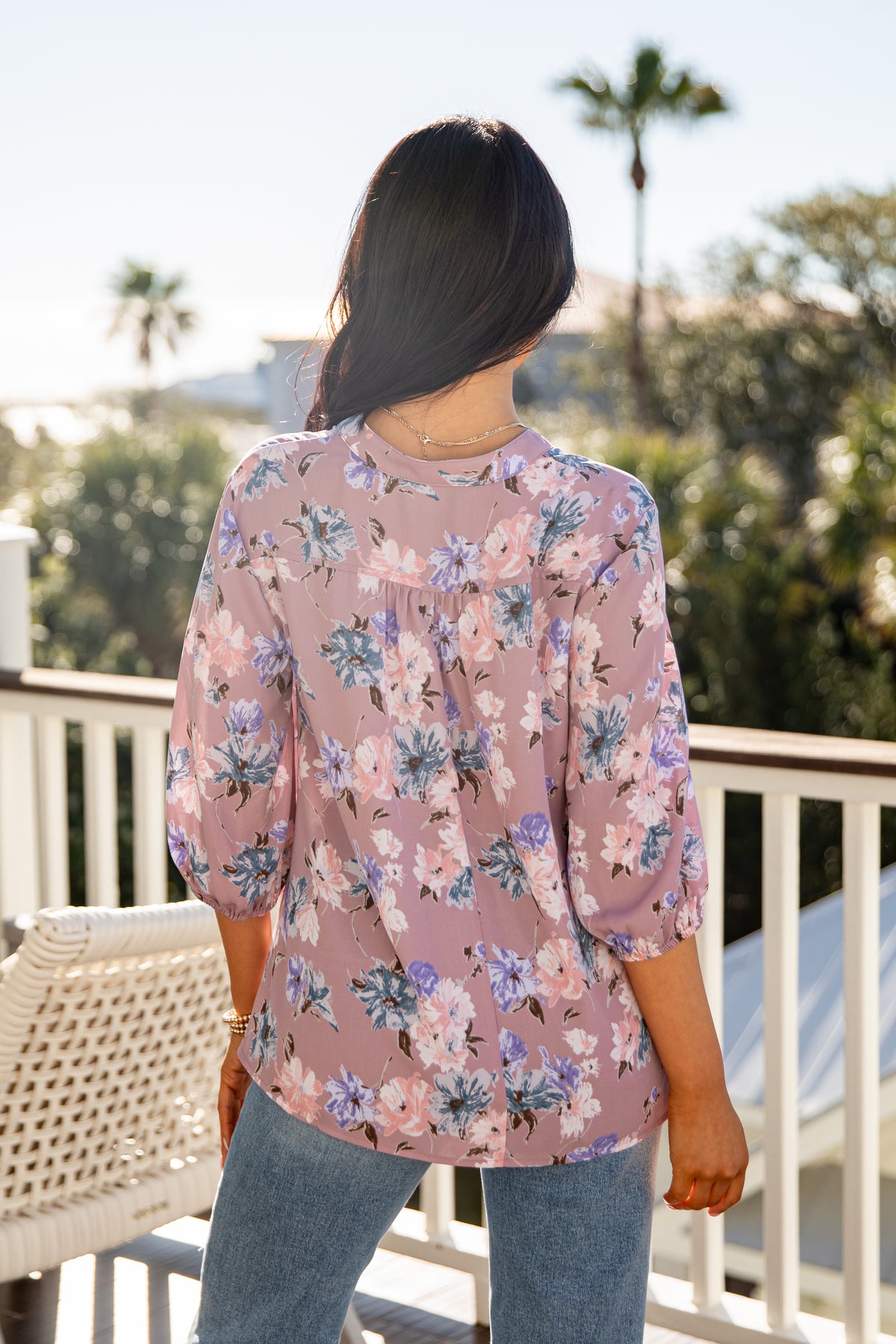 Person wearing a floral blouse on a balcony with palm trees in the background